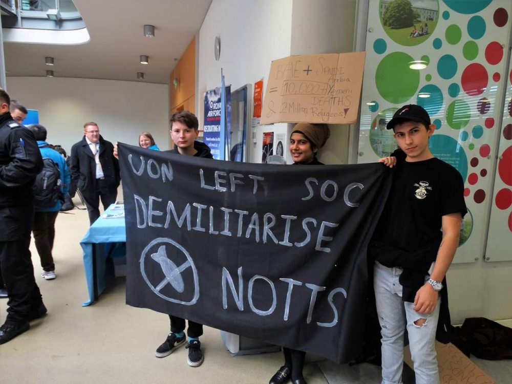 Students hold a banner outside careers fair arms company stall which reads 'UON LEFT SOC DEMILITARISE NOTTS'