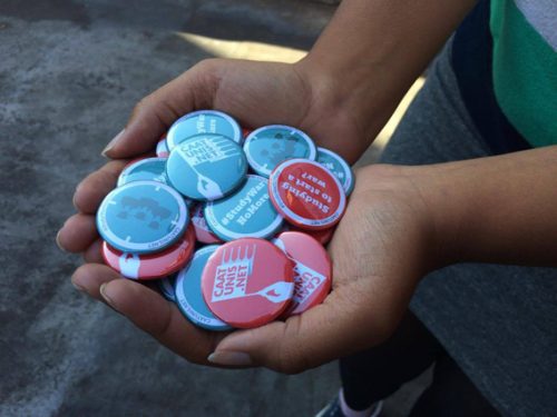 Hand holding out Campaign Against Arms Trade Universities Network badges