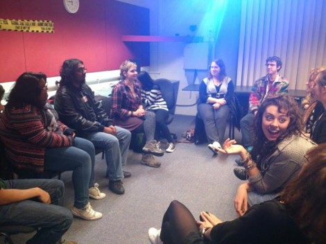 Group of young people, sitting on chairs in a circle, having a discussion.